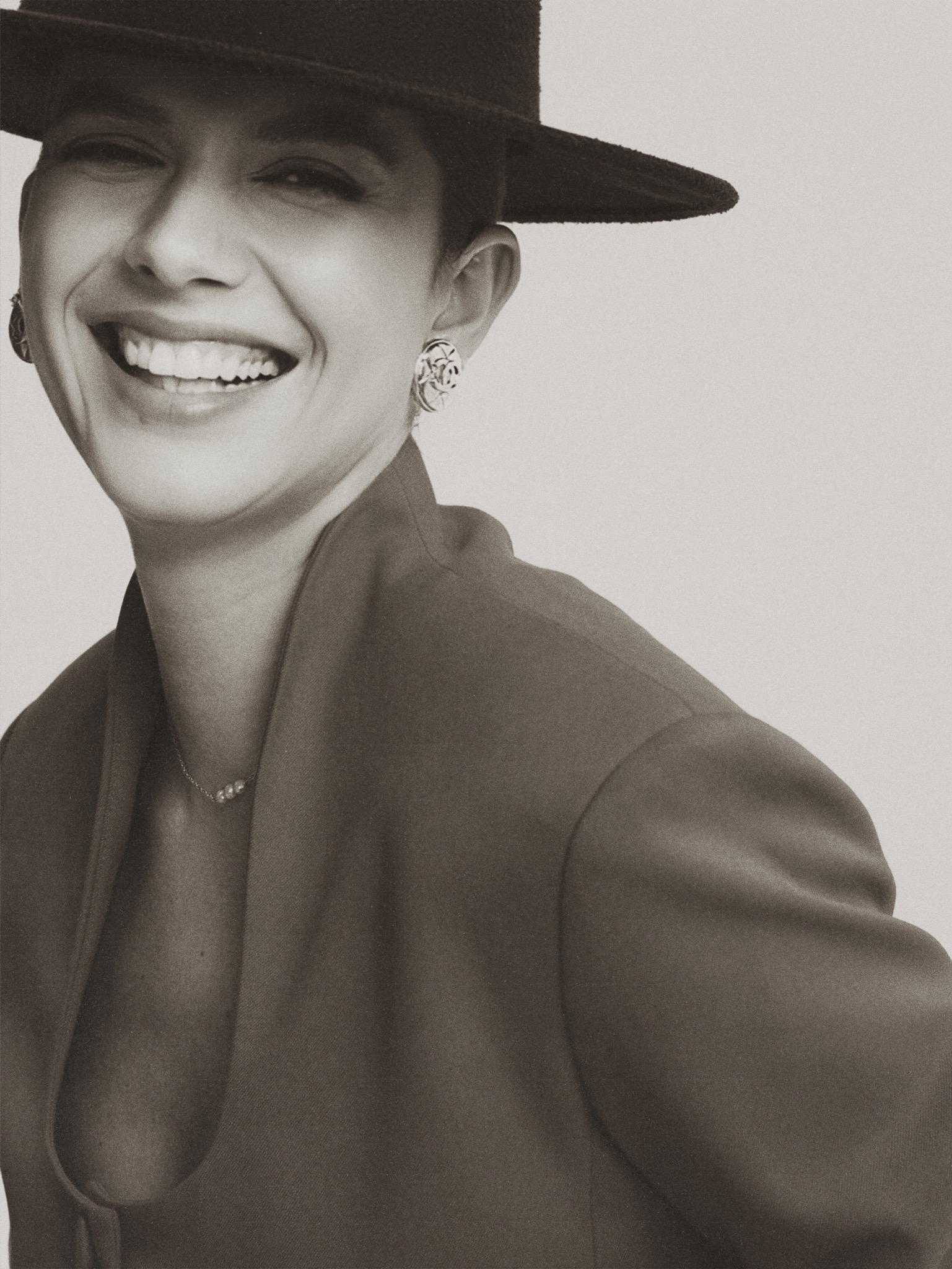 Portrait of the live workshop host smiling in a wide-brim hat and tailored jacket.